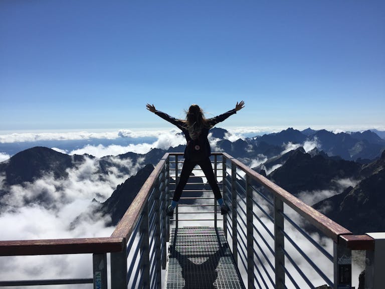 A woman stands on a viewing platform in Vysoké Tatry, Slovakia, surrounded by clouds and mountains, embracing freedom.