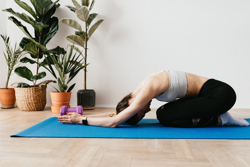 Side view full length anonymous sporty lady in activewear stretching in Child Pose on yoga mat during post workout stretch at home