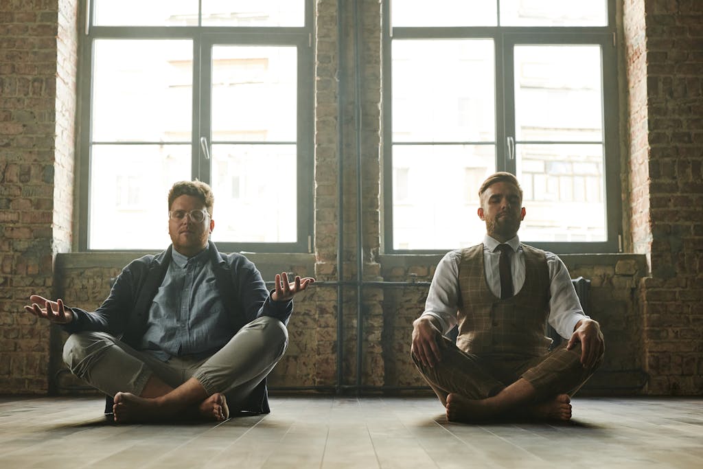 Two men meditating indoors in a loft with natural light, promoting relaxation and mindfulness.